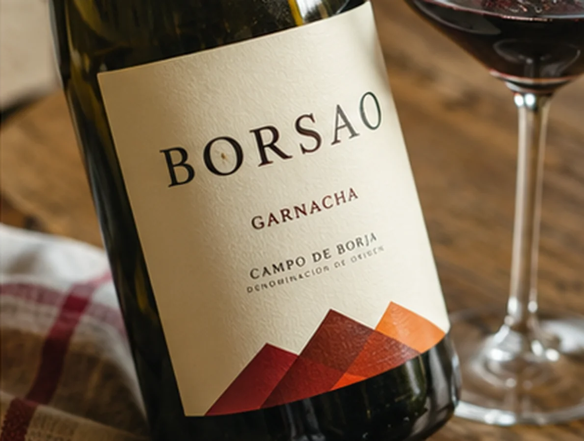 Close-up of an opened Borsao Garnacha bottle beside a glass of red wine on a wooden table.