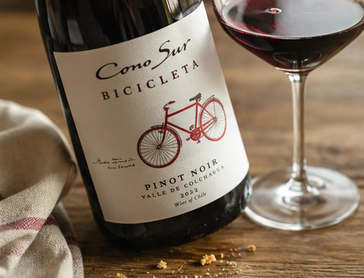 Close-up of a Cono Sur Bicicleta Pinot Noir bottle beside a glass of ruby red wine.